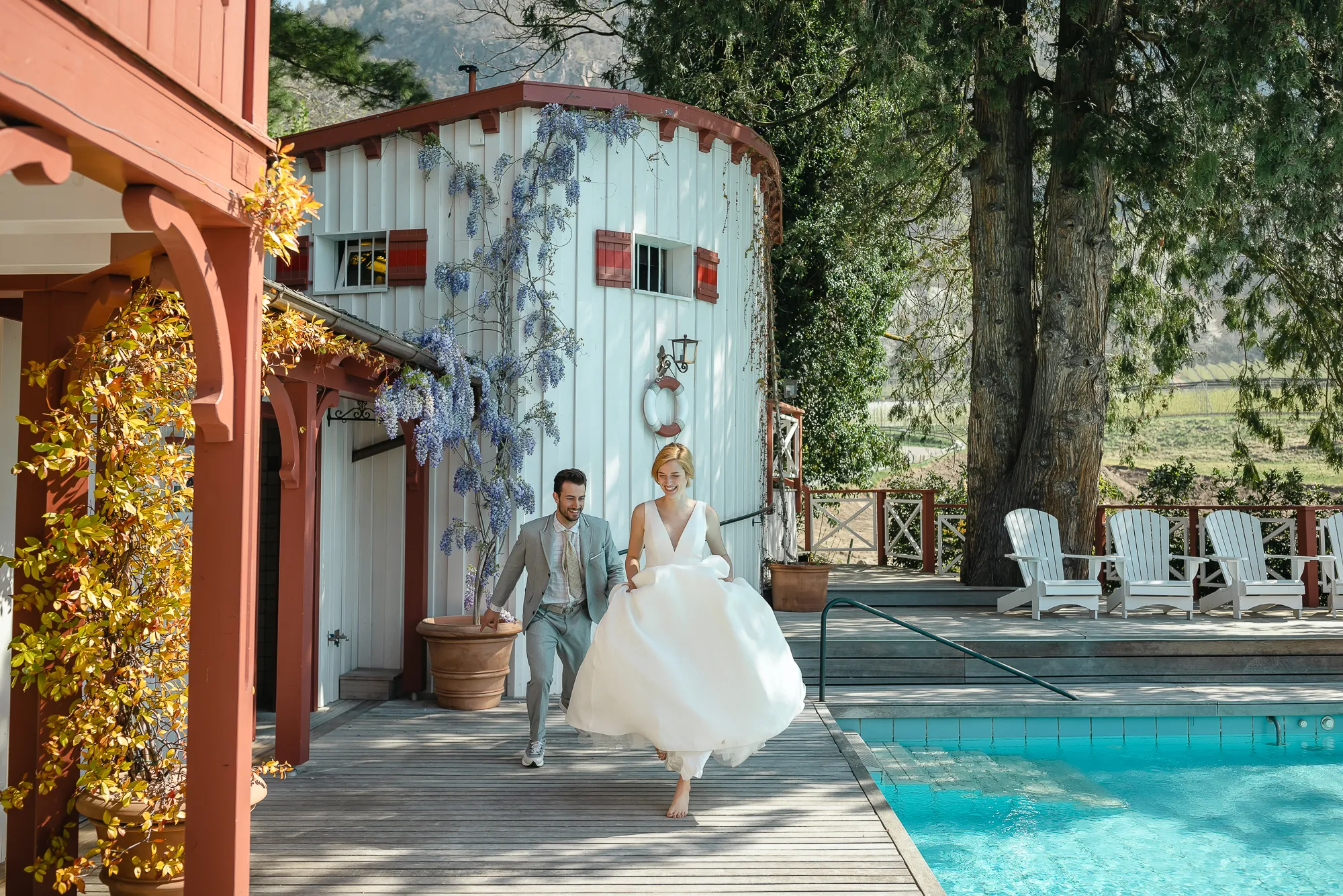 Happy couple in wedding attire runs towards pool at Relais & Châteaux Castel Fragsburg. Italian wedding.