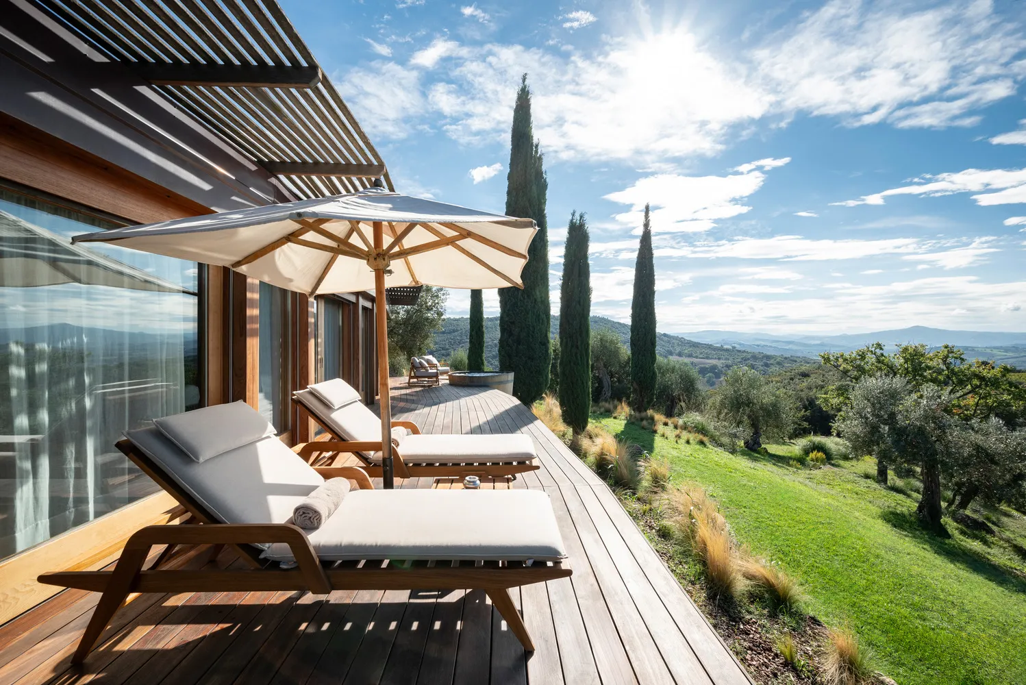 Luxury lounge chairs on a wooden deck overlooking Tuscan countryside.