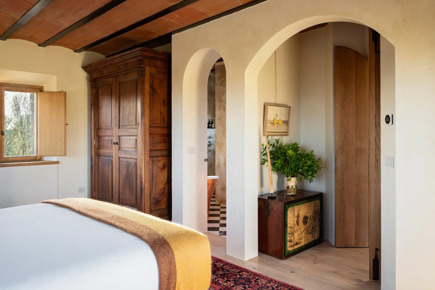 Luxurious bedroom suite at Castello Di Vicarello, featuring an antique wardrobe and arched entryway to ensuite bathroom. Ideal castle wedding venue.