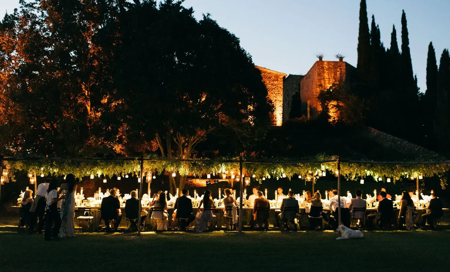 Romantic outdoor wedding reception at Castello Di Vicarello, a stunning castle wedding venue. Guests dine under a canopy of greenery and lights.