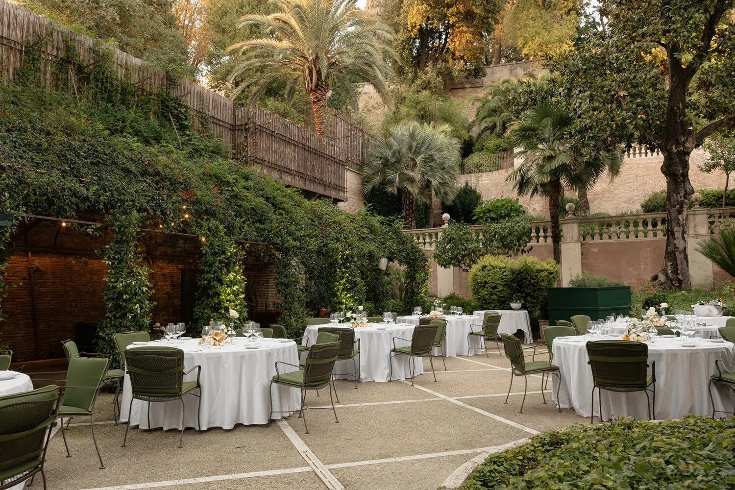 Elegant outdoor wedding reception at Hotel De Russie in Rome. Tables with white linens and green chairs are set in a lush garden.