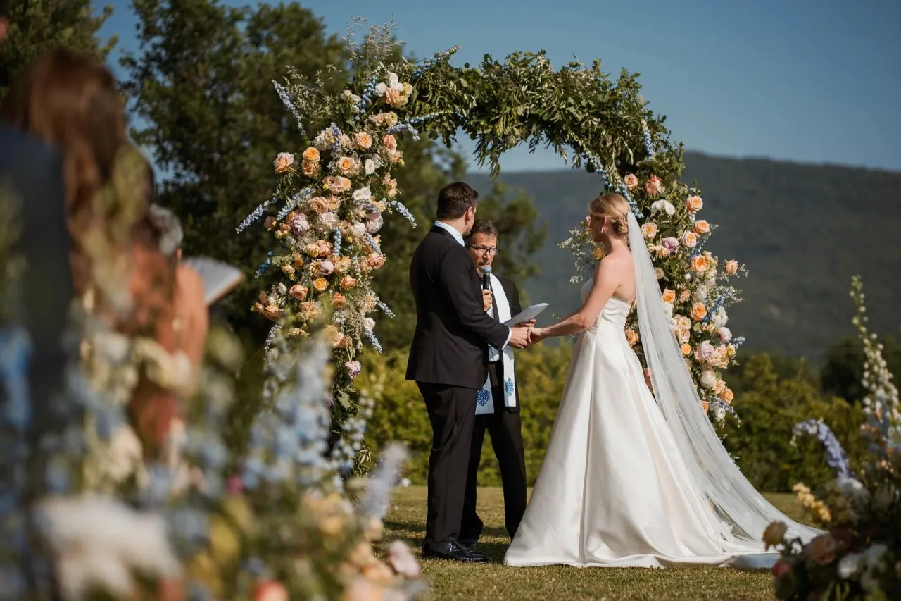 Bride and groom exchange vows during a romantic Italian countryside wedding ceremony under a floral arch.