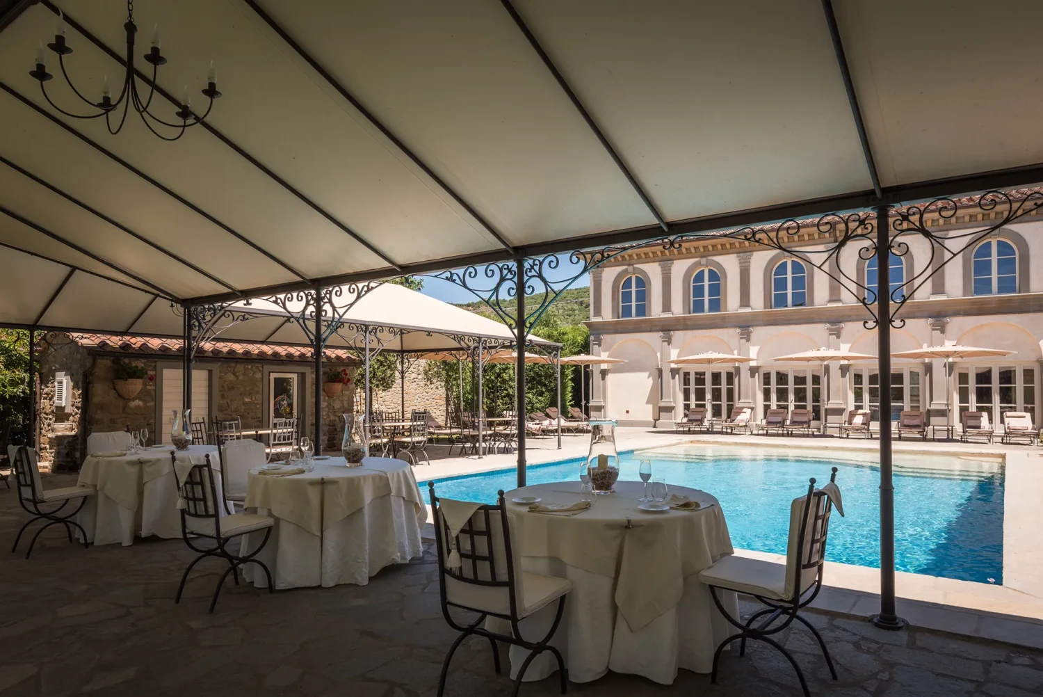 Elegant outdoor dining area with tables set for an Italian countryside wedding near a sparkling pool.