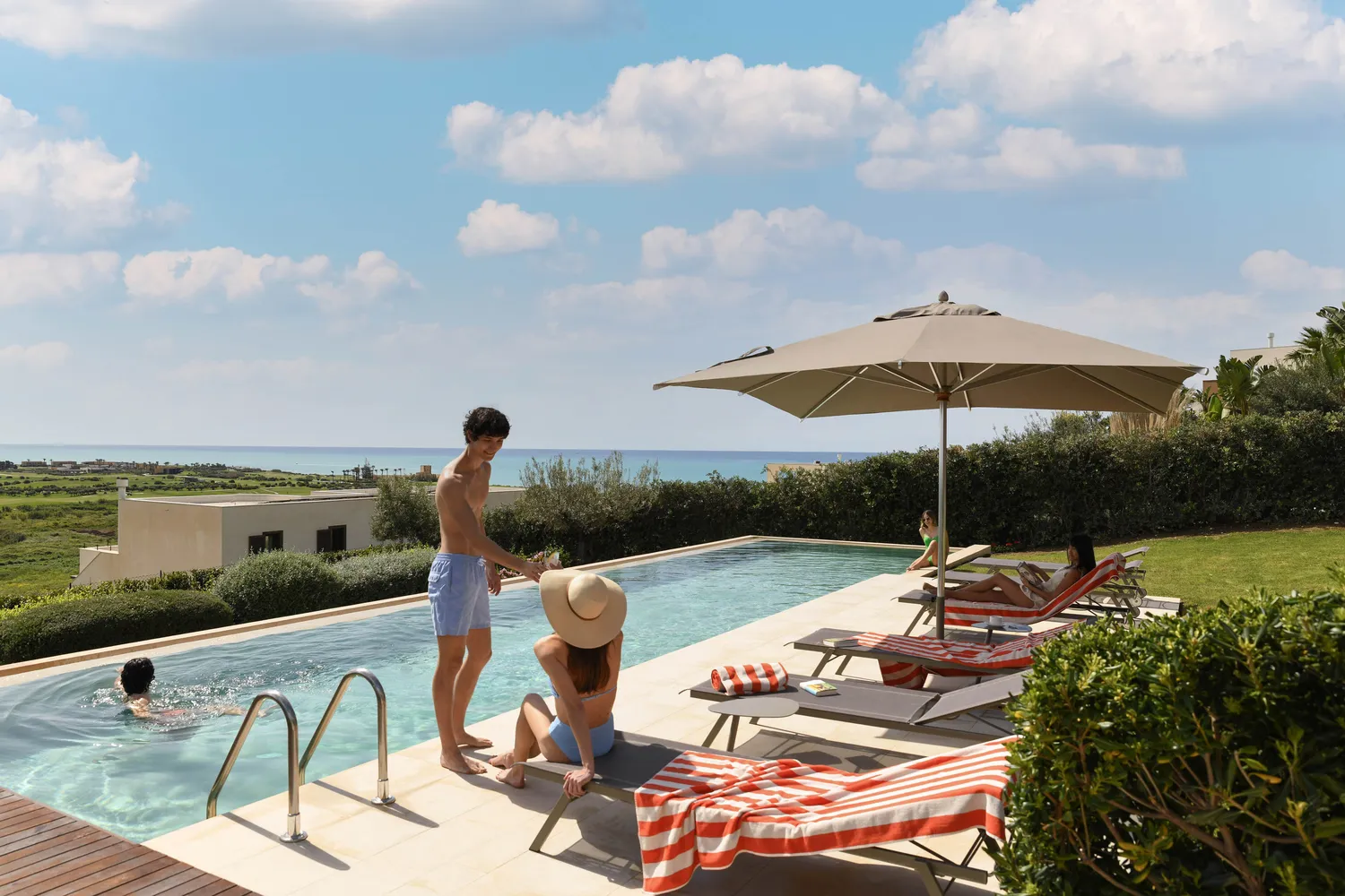 Family relaxing by a resort pool overlooking the sea in Sicily.