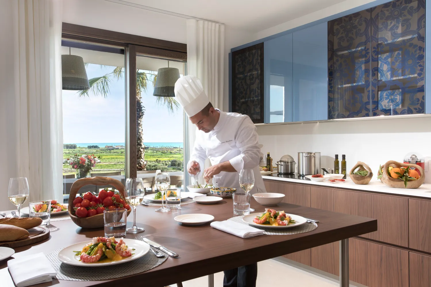 Chef preparing a meal in a luxurious Sicily kitchen overlooking the sea. Perfect for a Verdura Resort destination wedding.