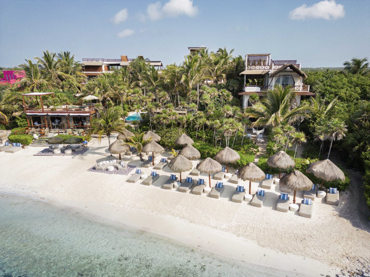 Jashita Hotel Tulum beachfront view with thatched umbrellas and lounge chairs on white sand.