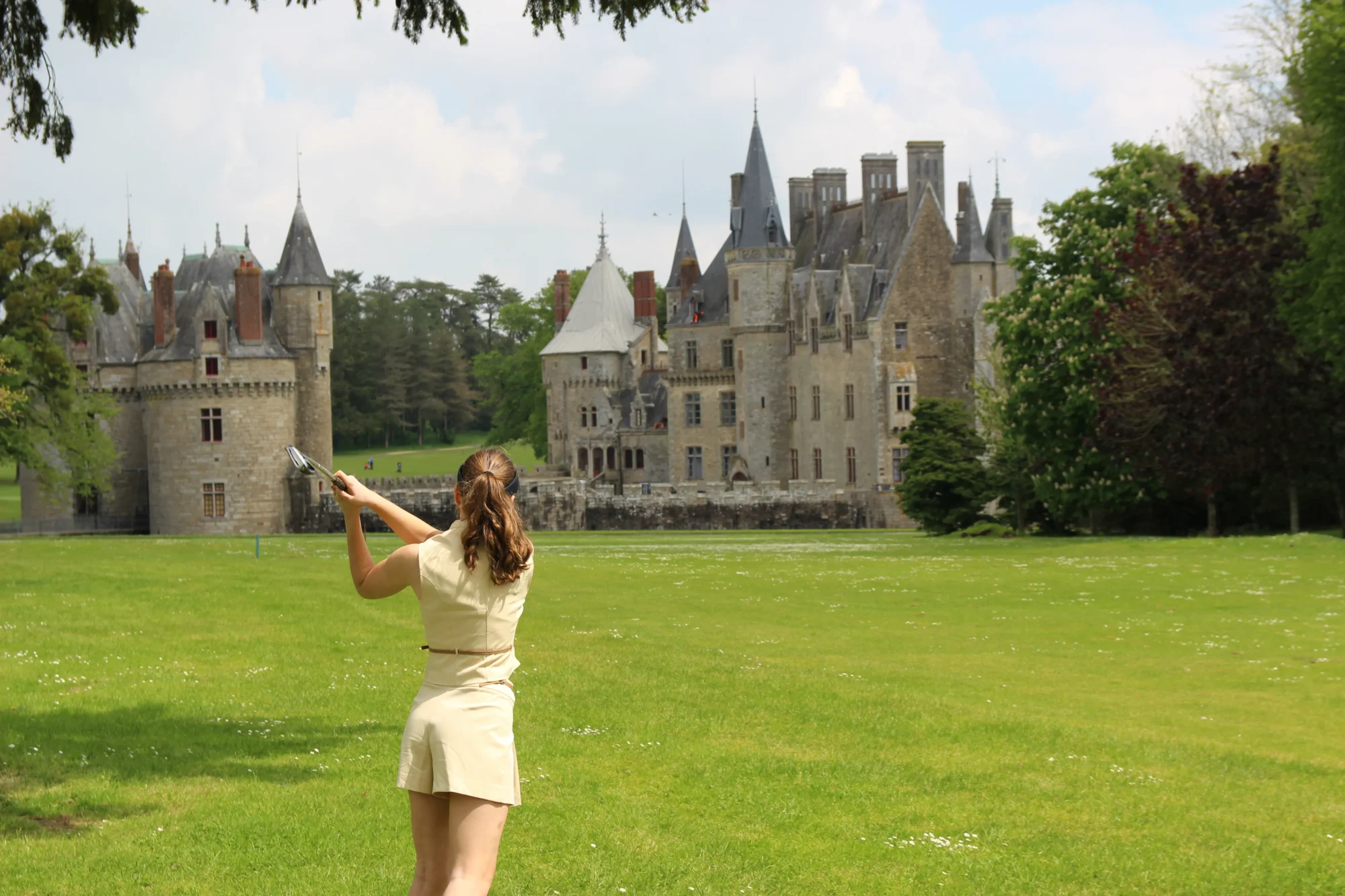 Woman playing golf with a French castle, Domaine de la Bretesche, in the background.