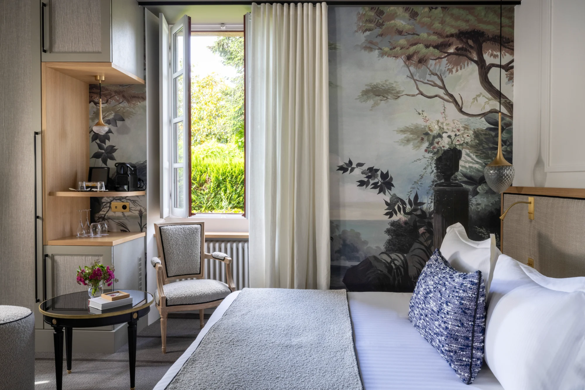 Elegant bedroom in a French chateau, featuring a scenic mural and comfortable seating.