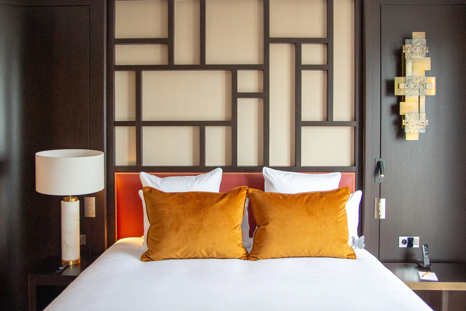 Luxurious hotel bedroom with orange pillows and a geometric headboard. Romantic Paris setting.
