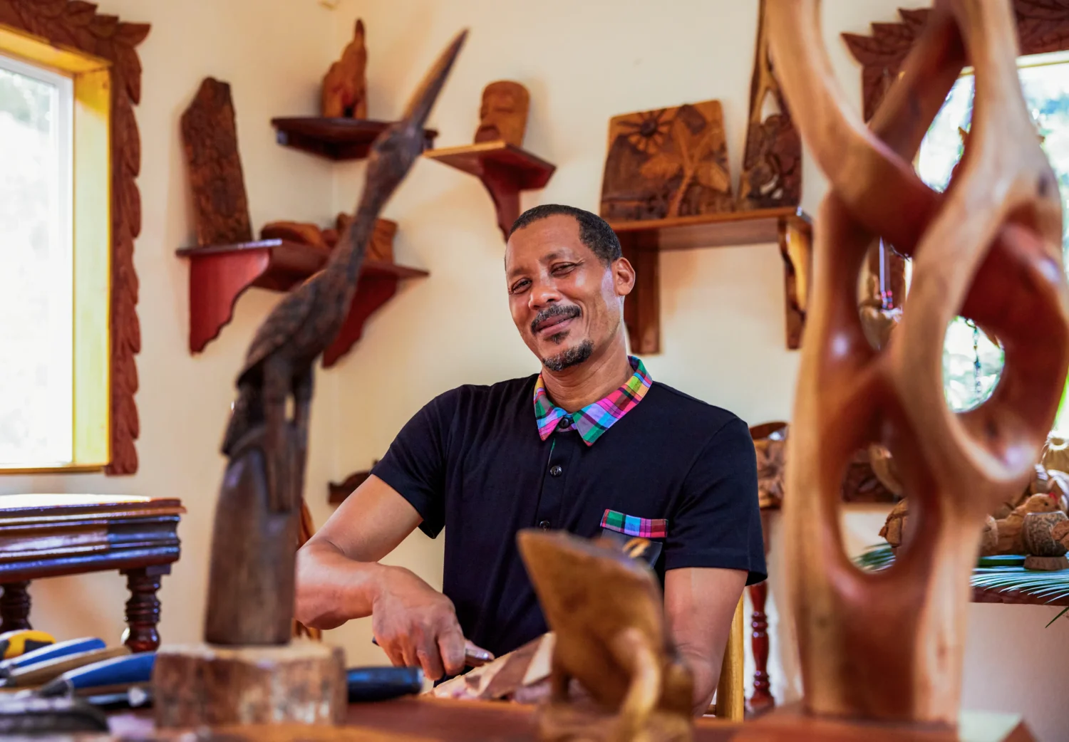 Smiling woodcarver in his studio, surrounded by handcrafted sculptures.