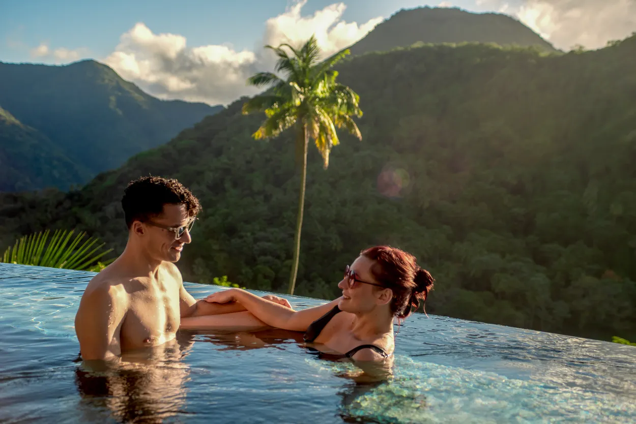 Couple relaxing in infinity pool overlooking lush green mountains at Ladera Resort, perfect for an island honeymoon.