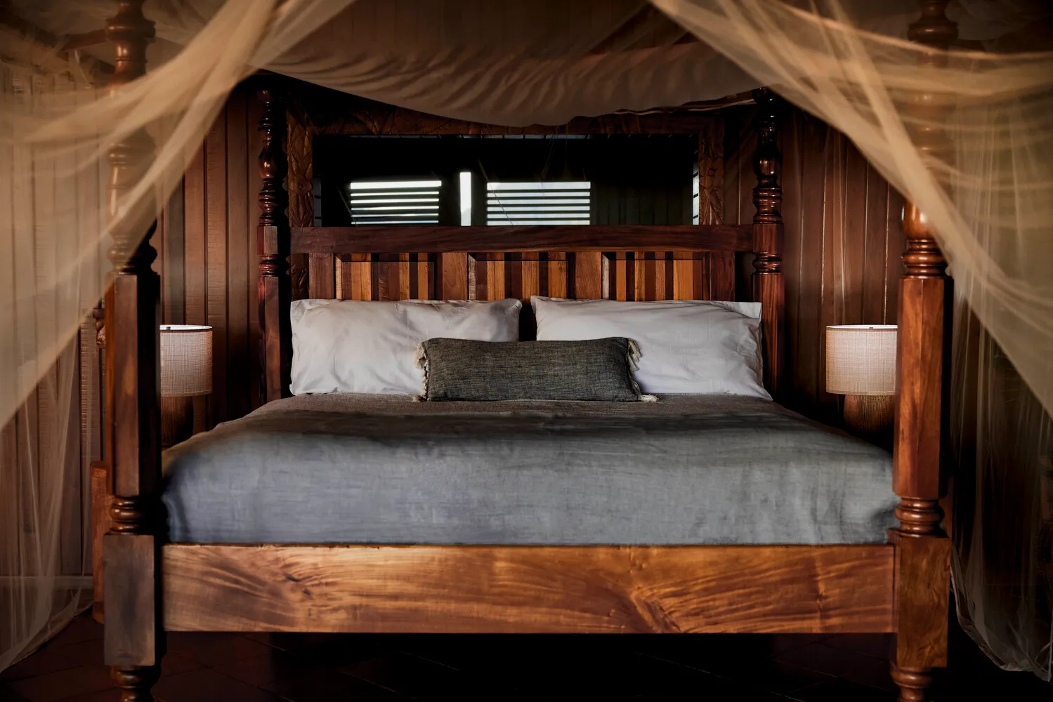 Luxurious four-poster bed with mosquito netting in a wooden room. Perfect for an island honeymoon at Ladera Resort.