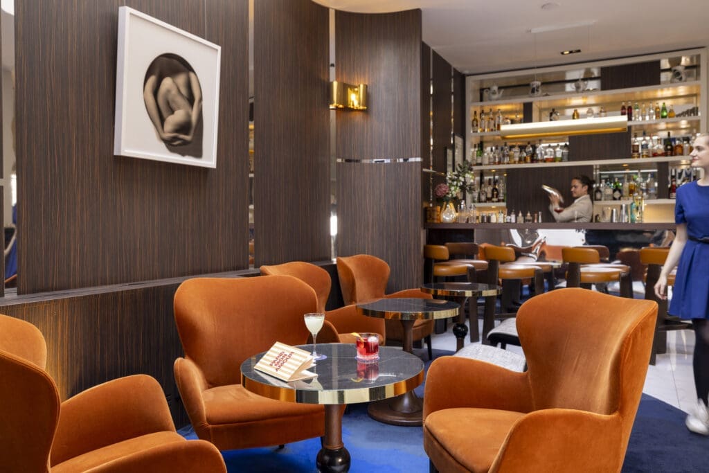 Luxurious lounge area at the Hotel Bel Ami, a chic Paris honeymoon hotel. Orange armchairs and a marble-top table.