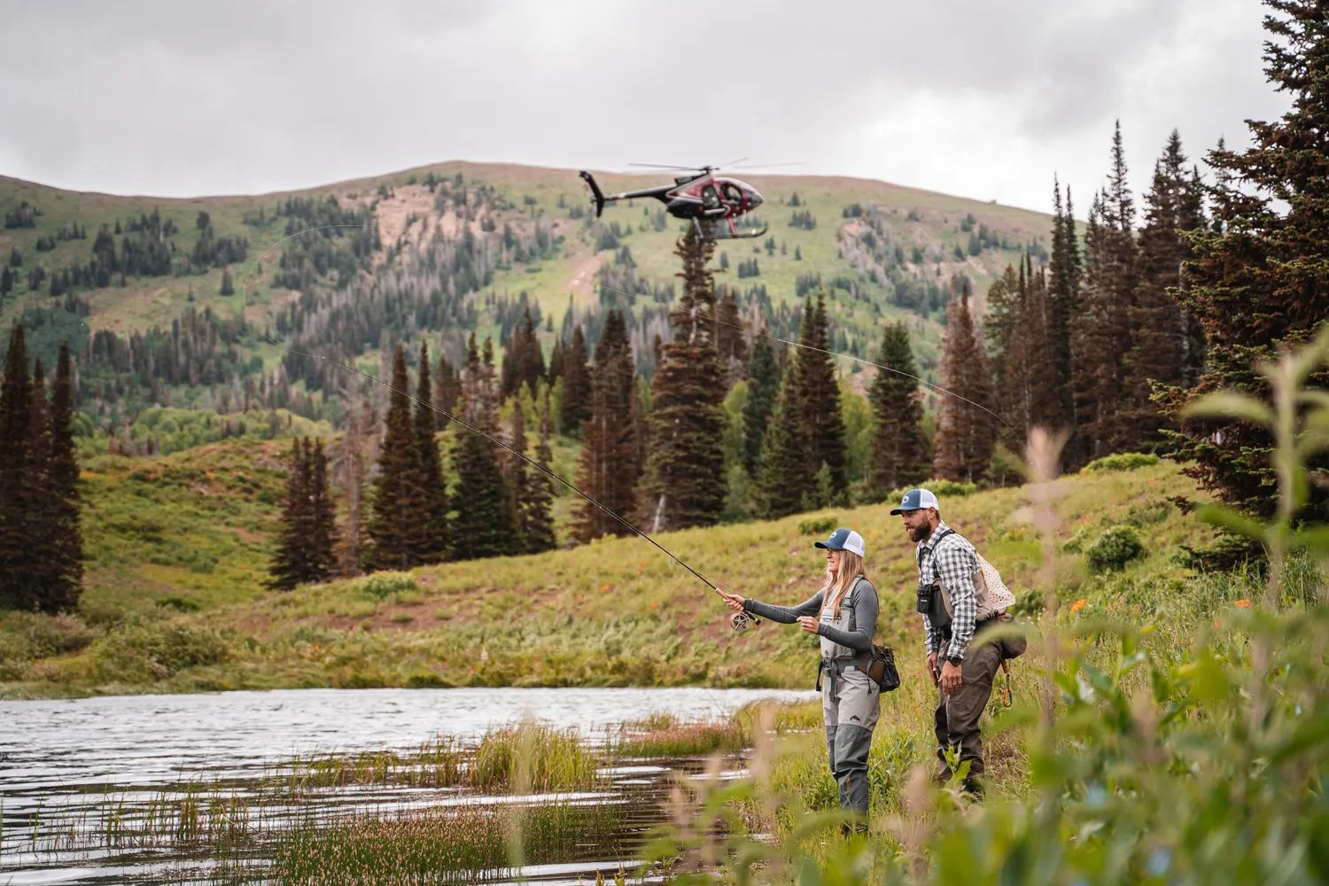 Couple fly fishing in a scenic Utah location, with a helicopter in the background.