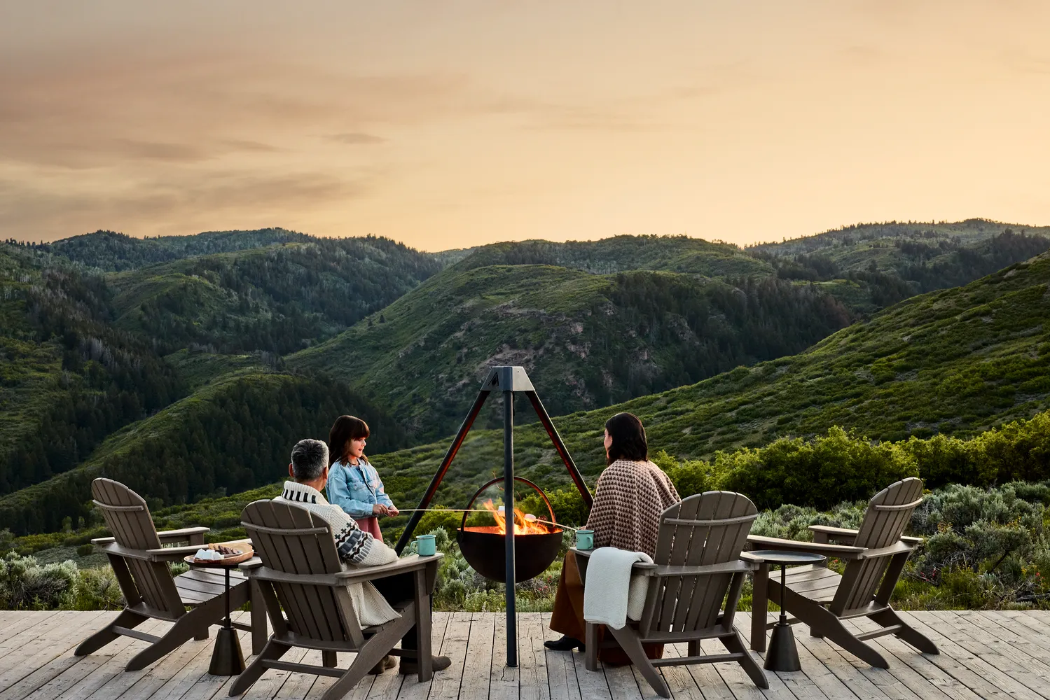 Family roasting marshmallows around a fire pit on a deck overlooking a Utah mountain range.