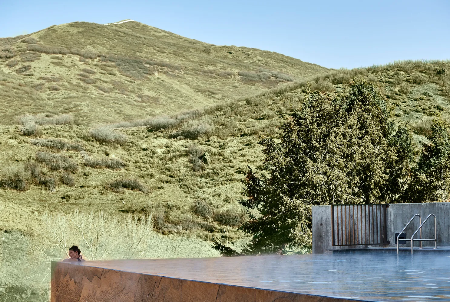 Woman relaxing in a hot spring pool overlooking a Utah mountain range. Lodge at Blue Sky.