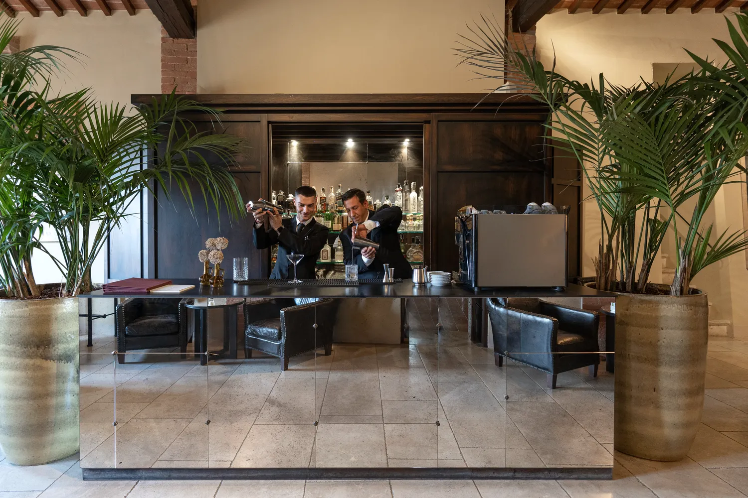 Two bartenders prepare cocktails at a stylish bar in Tuscany. Perfect for a Castel Monastero wedding or honeymoon.