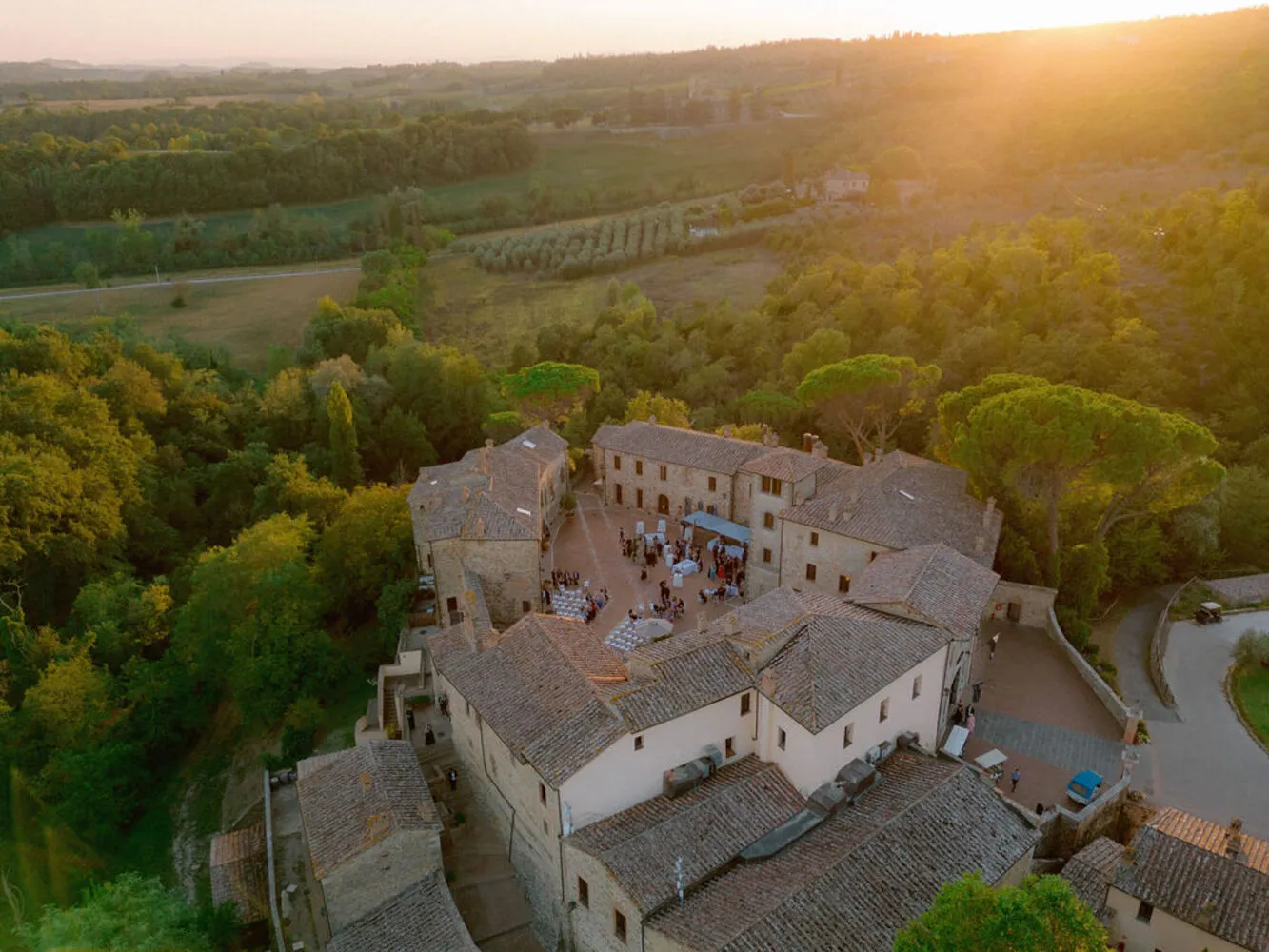 Aerial view of Castel Monastero in Tuscany, Italy. Guests enjoy a wedding reception in the courtyard.