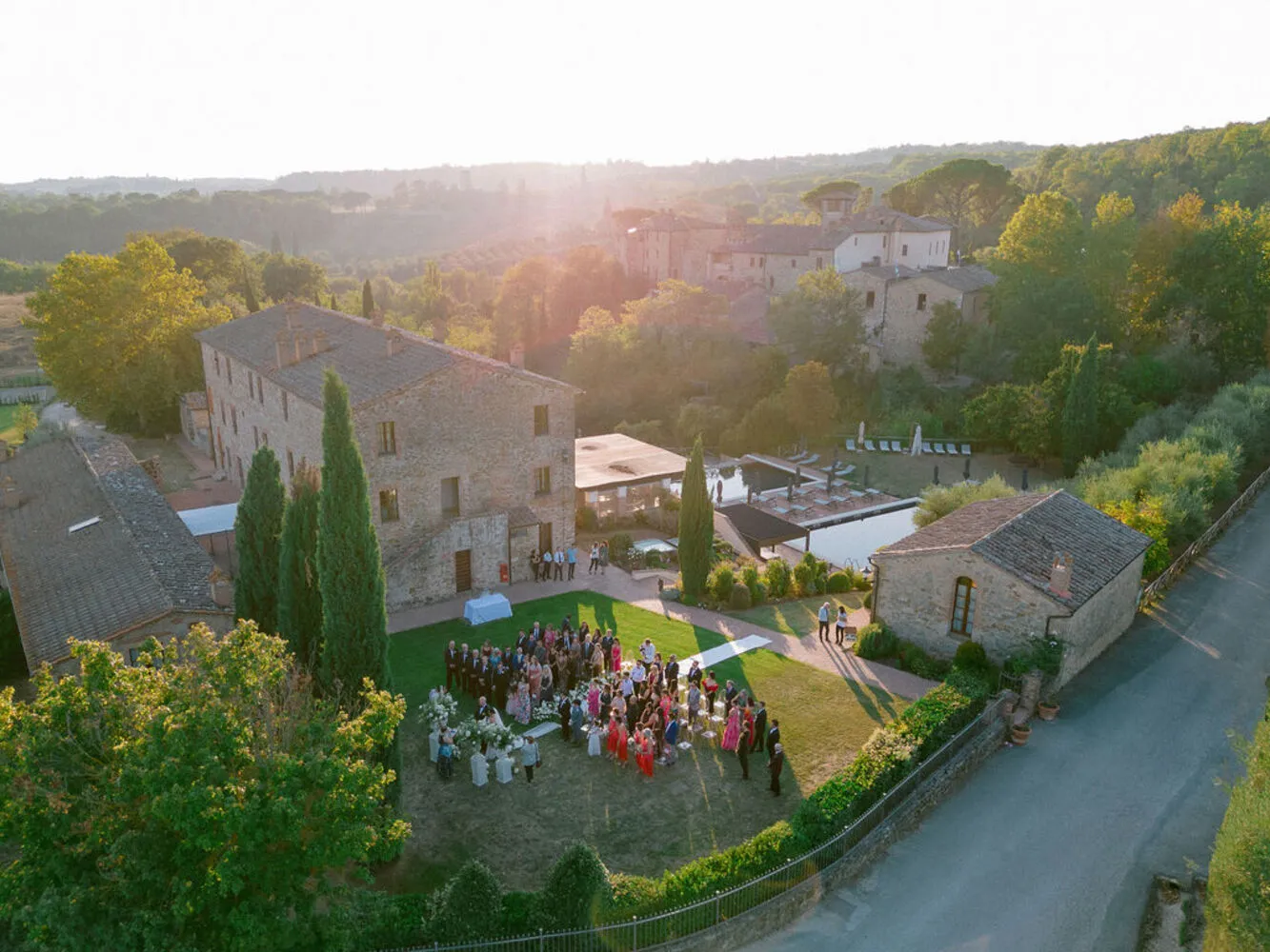 Aerial view of a Tuscany wedding at Castel Monastero. Guests gather for the ceremony on the lawn.