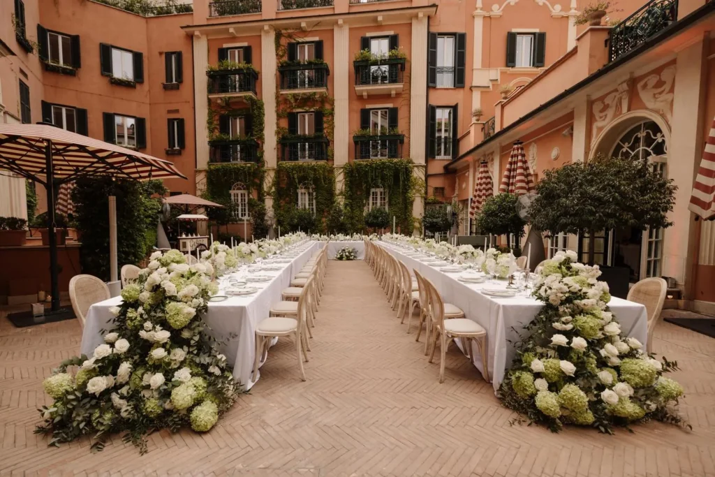 Elegant wedding reception at Hotel de la Ville, Rome. Long tables adorned with lush white and green floral arrangements.