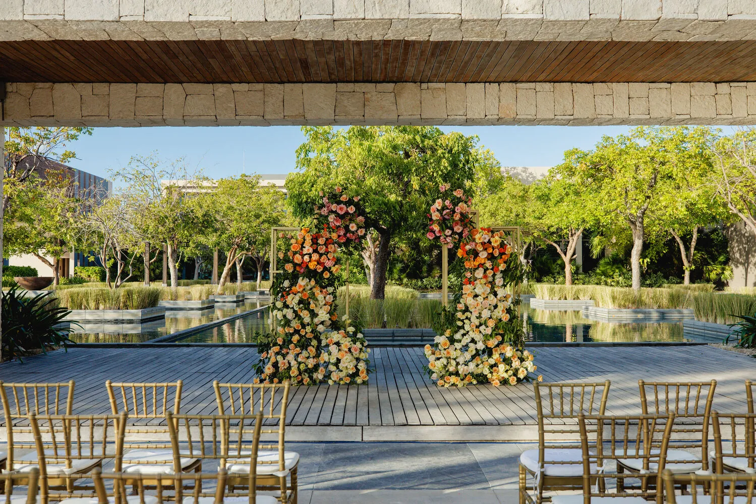 Luxury Cancun wedding ceremony setup at NIZUC Resort & Spa, featuring a floral arch and gold chairs.