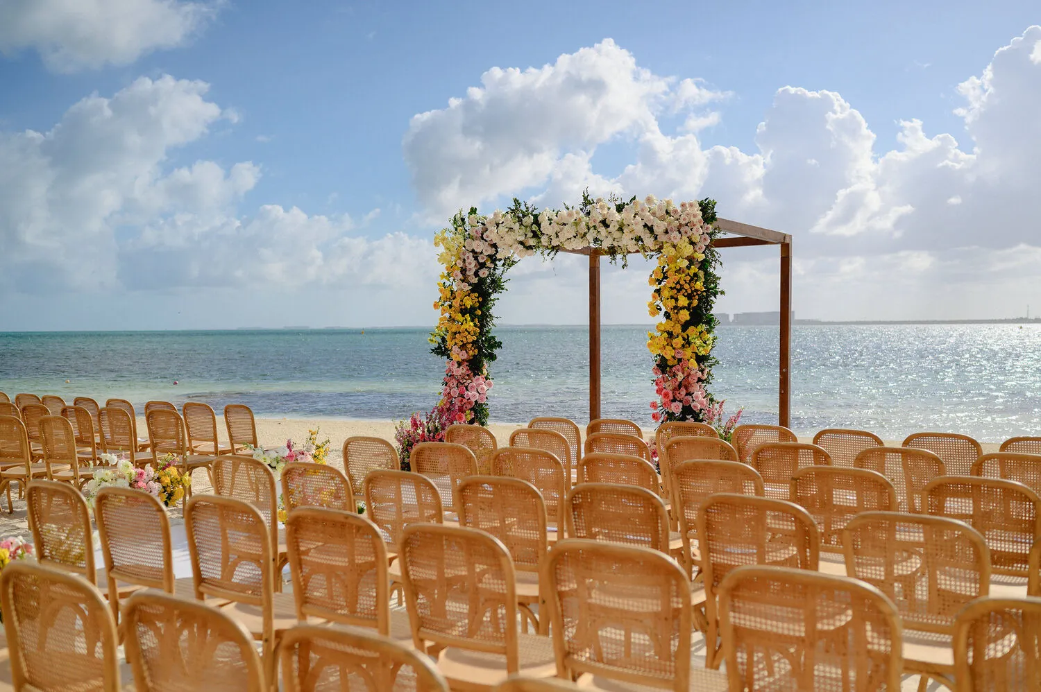 Beach wedding ceremony setup at NIZUC Resort & Spa in Cancun. Floral arch and chairs face ocean.