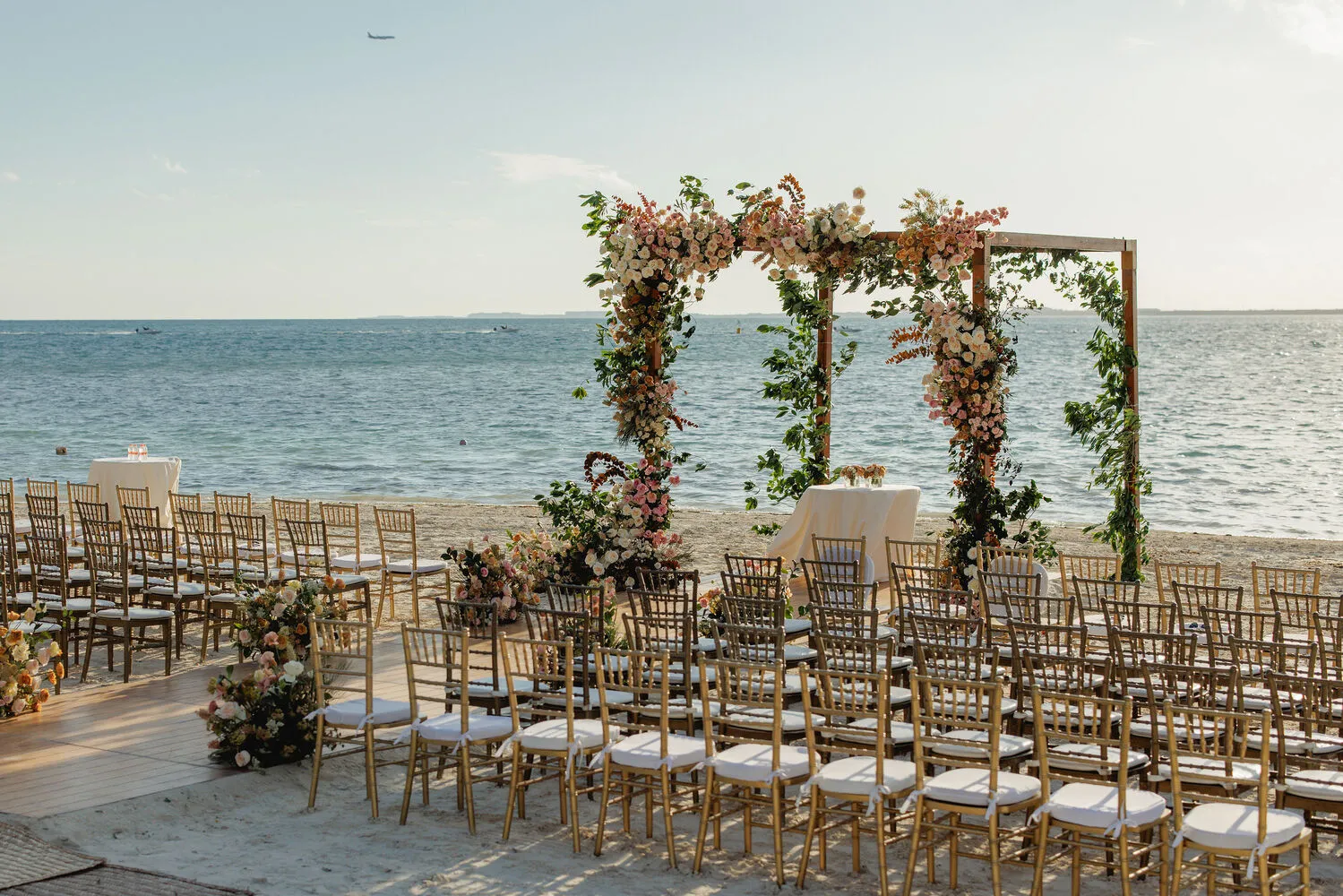 Beach wedding ceremony setup at NIZUC Resort & Spa in Cancun. Gold chairs face a floral archway overlooking the ocean.