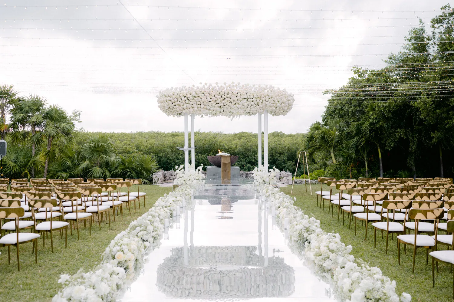 Elegant outdoor wedding ceremony at NIZUC Resort & Spa in Cancun. White floral archway and gold chairs.