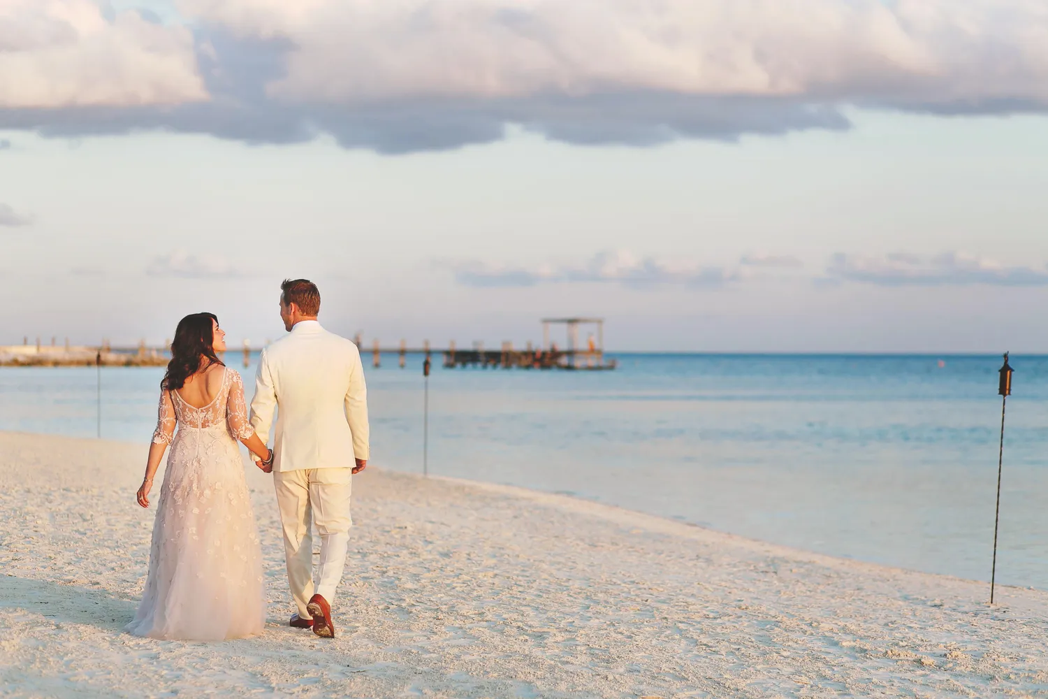 Bride and groom holding hands, walking on a Cancun beach at sunset. NIZUC Resort & Spa wedding.