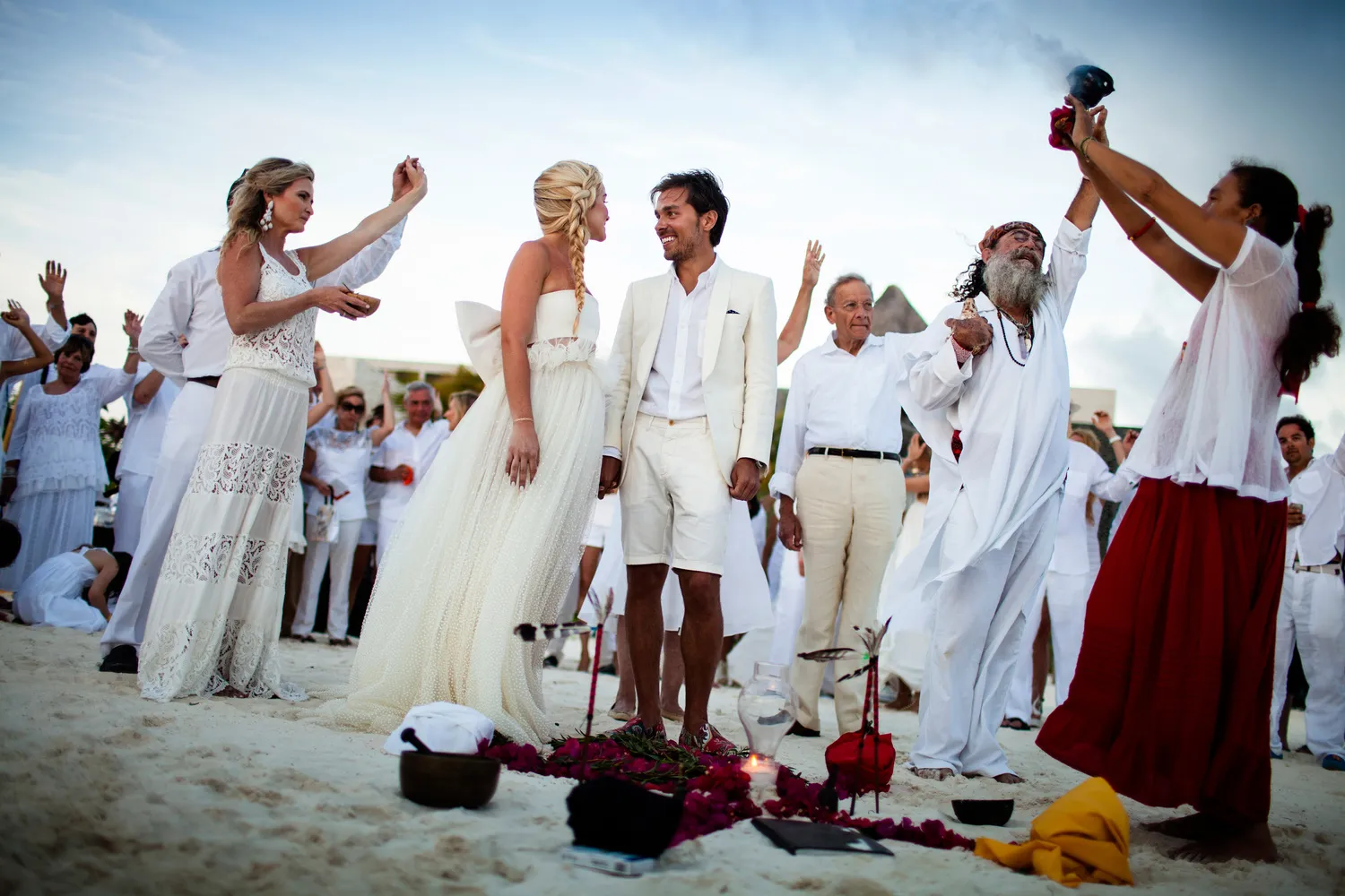 Couple exchanging vows in a beach wedding ceremony at NIZUC Resort & Spa in Cancun. Guests in white attire witness the special moment.