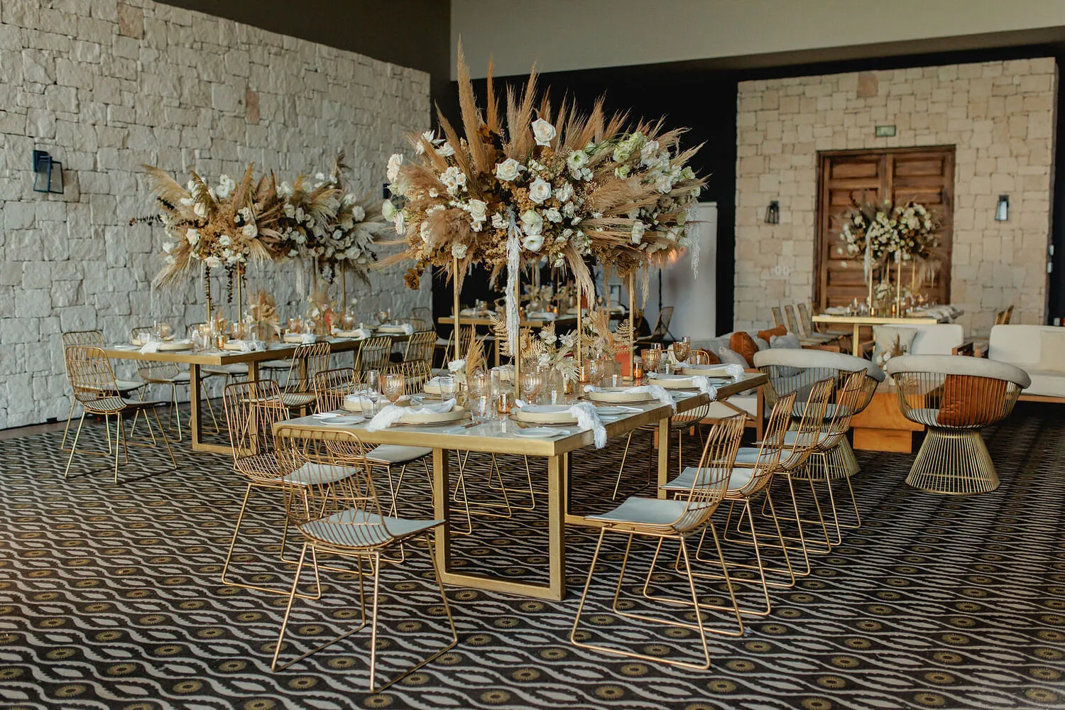 Elegant gold chairs and tables adorned with pampas grass and white rose centerpieces at a Cancun wedding reception at NIZUC Resort & Spa.