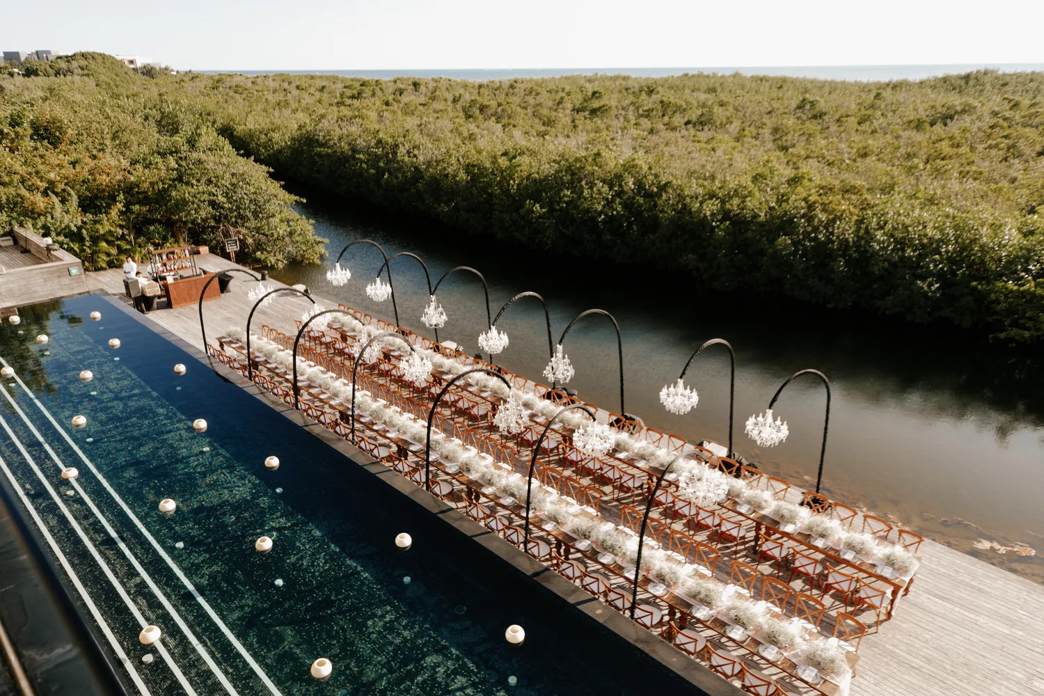 Elegant Cancun wedding reception at NIZUC Resort & Spa, featuring long tables with floral centerpieces and chandeliers over a pool.