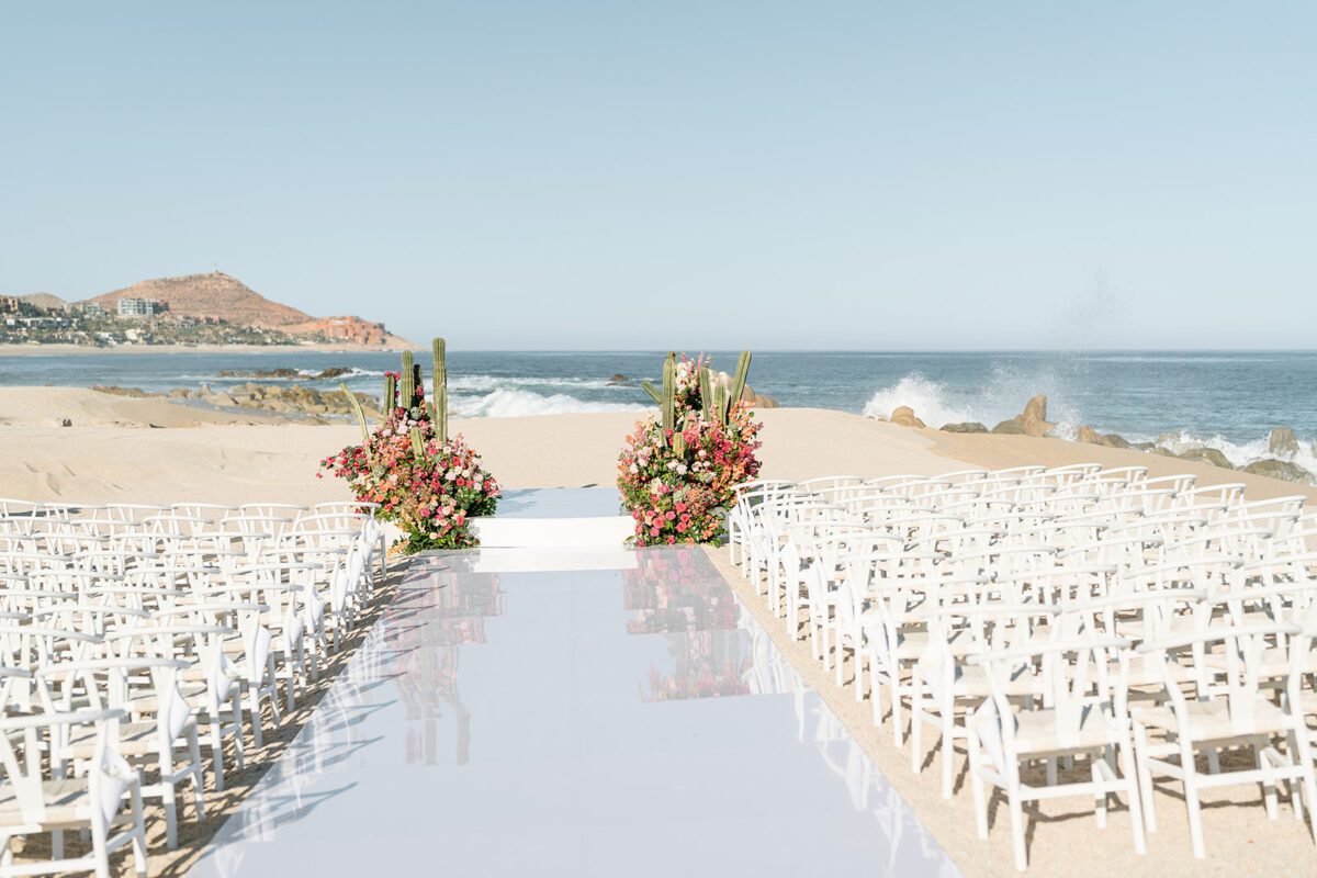 Los Cabos destination wedding setup on the beach with white chairs and floral arrangements.