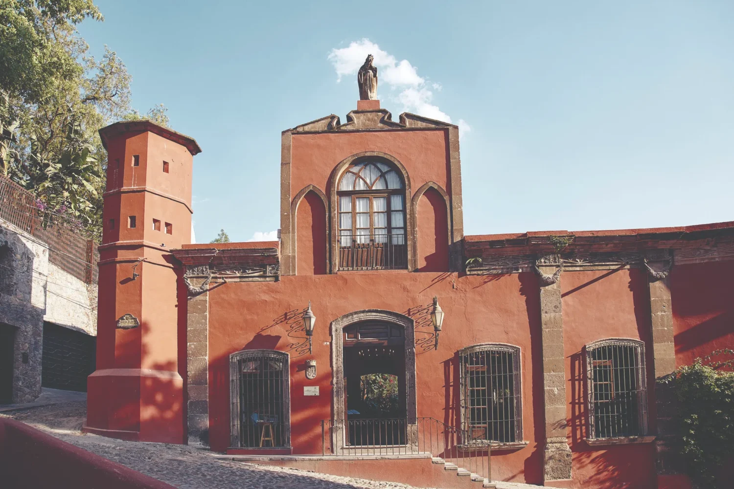 Historic Casa de Sierra Nevada building in San Miguel de Allende, featuring a red facade, arched windows, and a statue atop.