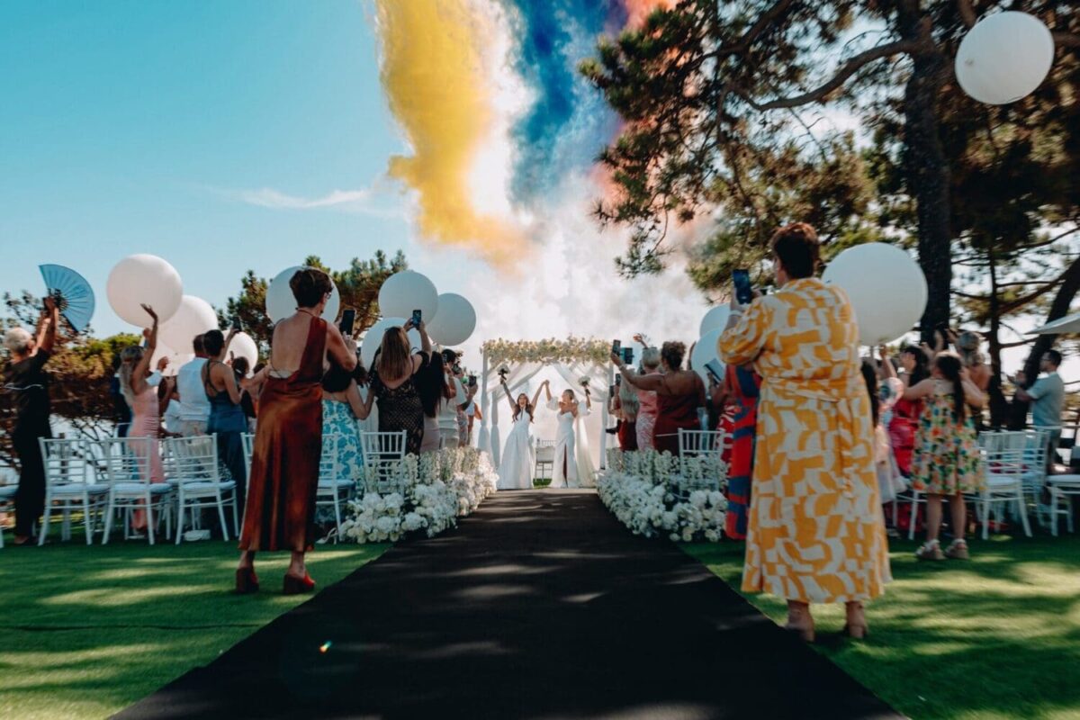 Two brides joyfully celebrate at their Portugal destination wedding at W Algarve, amidst cheering guests and colorful smoke.