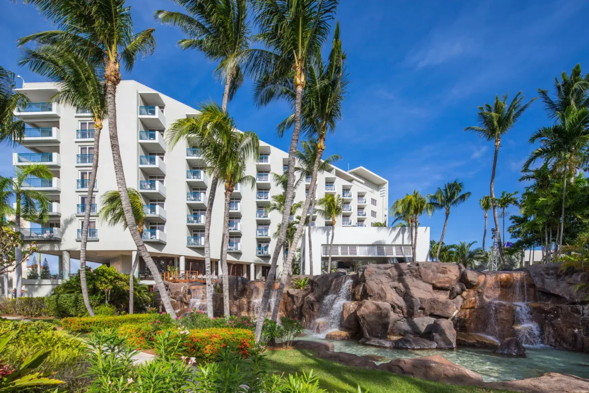Hilton Aruba Caribbean Resort with waterfalls and palm trees under a bright blue sky. Perfect for a Hilton Aruba Destination Wedding.