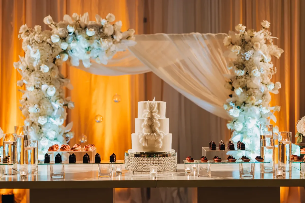 Elegant wedding cake display at a Hilton Aruba Destination Wedding with floral arch and desserts