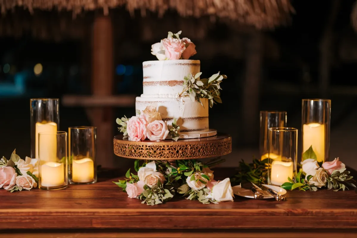 Elegant Hilton Aruba destination wedding cake with roses and candles on a wooden table