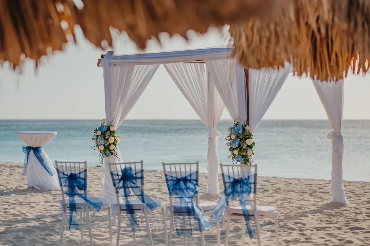 Beach wedding setup at Hilton Aruba Caribbean Resort, featuring a decorated arch and chairs; a perfect Hilton Aruba Destination Wedding location.