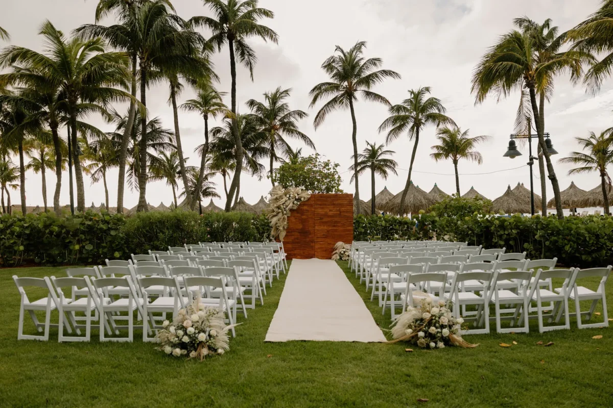 Wedding ceremony setup at Hilton Aruba Caribbean Resort with white chairs, aisle, and palm trees. Hilton Aruba Destination Wedding.