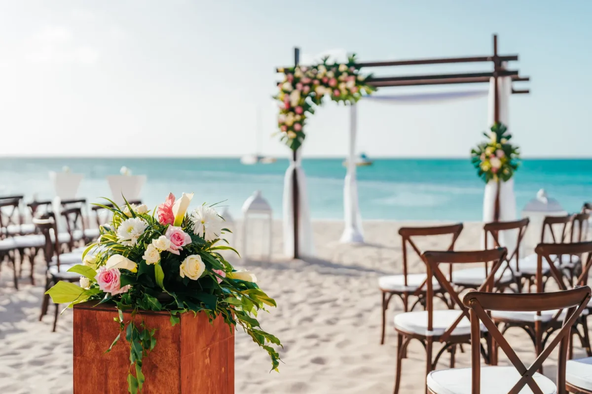 Beach wedding ceremony setup at Hilton Aruba Caribbean Resort, featuring floral arch and chairs. Hilton Aruba Destination Wedding.