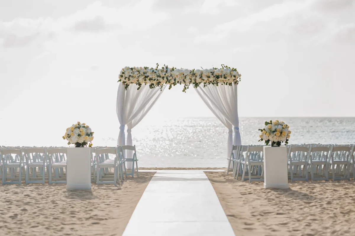Beach wedding ceremony at Hilton Aruba, featuring floral arch and white chairs. Perfect for a Hilton Aruba Destination Wedding.