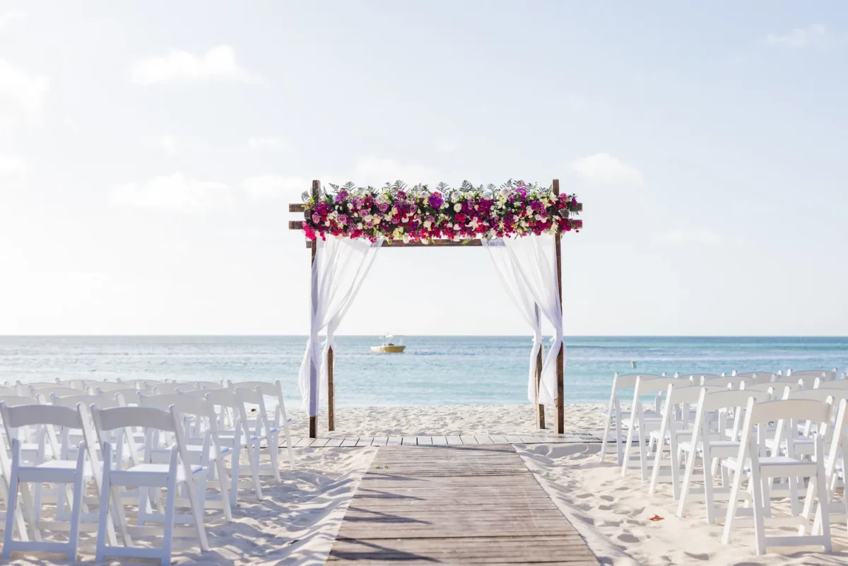 Beach wedding ceremony setup at Hilton Aruba Caribbean Resort, featuring a floral arch and white chairs. Perfect for a Hilton Aruba Destination Wedding.