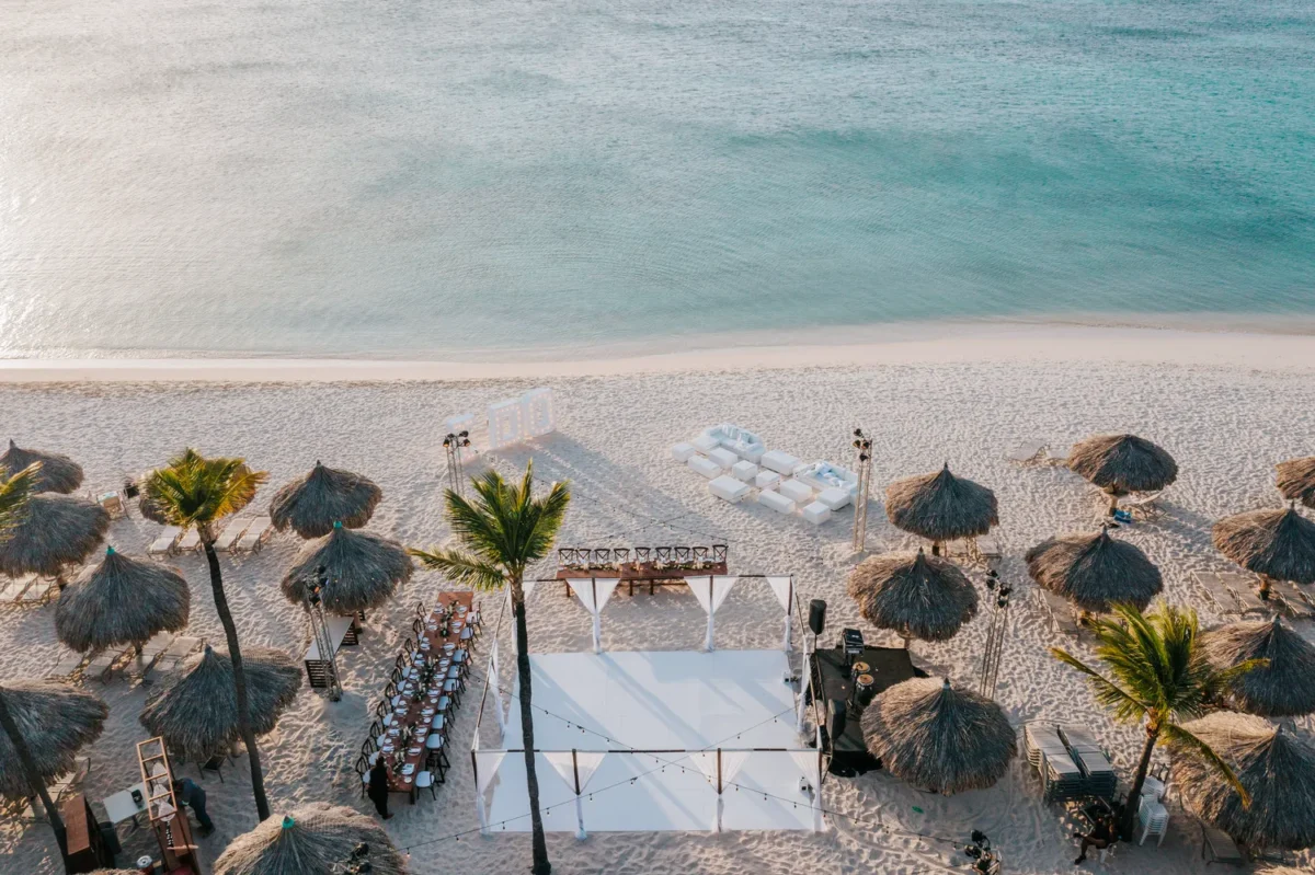 Beachfront Hilton Aruba Destination Wedding setup with ceremony stage and thatched umbrellas.