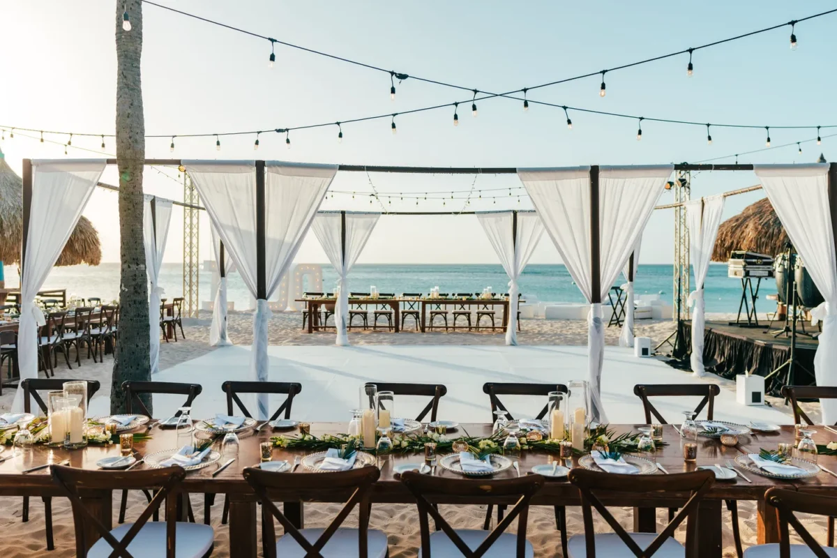 Beachfront Hilton Aruba Destination Wedding reception setup with long tables, string lights, and ocean view.
