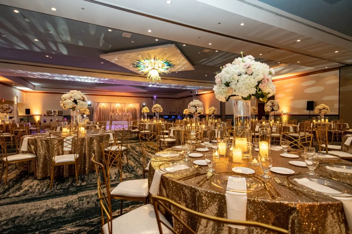 Elegant ballroom setup for a Hilton Aruba Destination Wedding with gold sequin tablecloths and floral centerpieces.