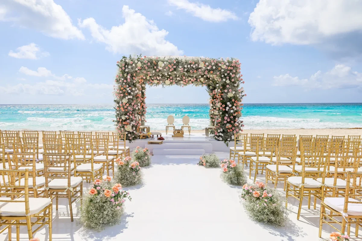 Beachfront destination wedding ceremony setup at Kempinski Hotel Cancún with floral arch and ocean view.