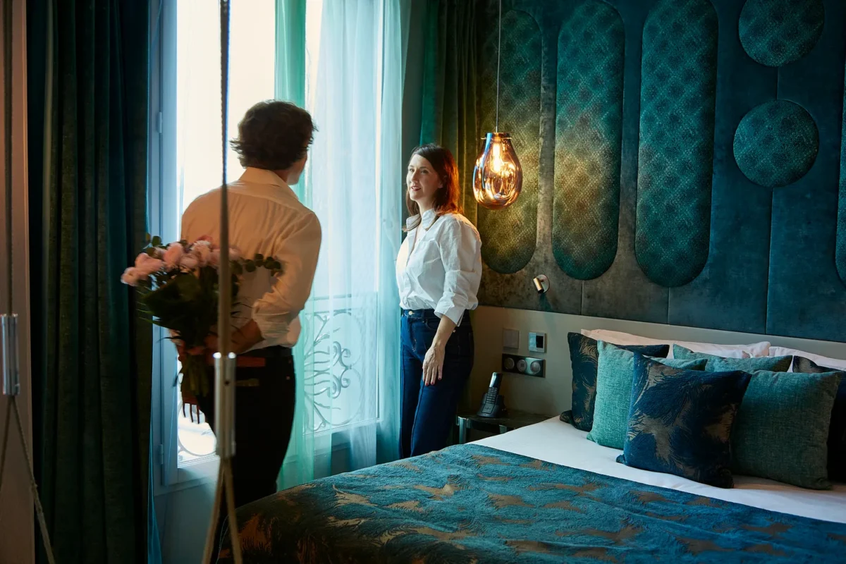 Couple in a Paris hotel room, he holds flowers. Romantic honeymoon getaway.
