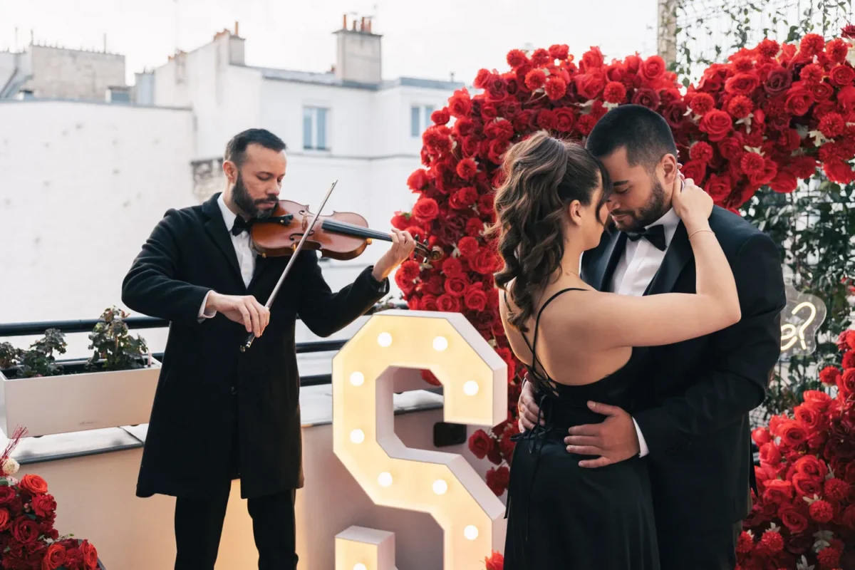 Romantic couple embraces on Paris rooftop, violinist plays. Paris destination honeymoon.