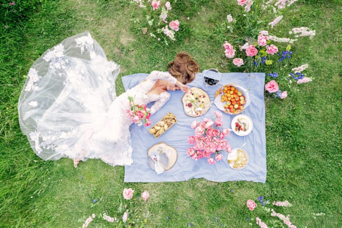 Bride in a white gown lying on picnic blanket with Italian cuisine and flowers